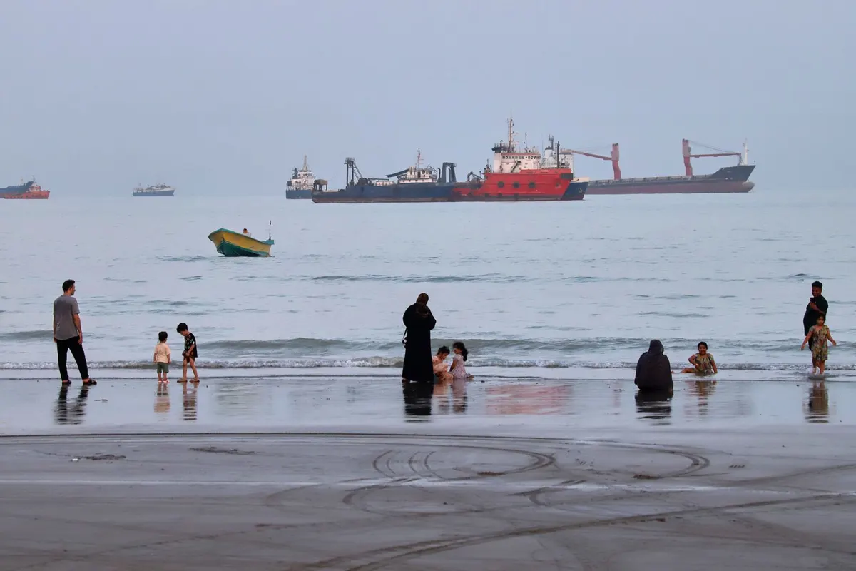 People spend time at a beach as commercial vessels are anchored in the Strait of Hormuz off Bandar Abbas, Iran, on August 5, 2026.