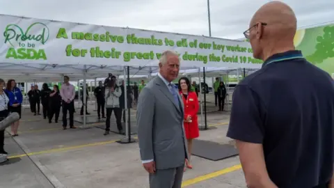AFP via Getty Images Then-Prince Charles in a grey suit speaks to a man with his back to the camera who is wearing Asda uniform